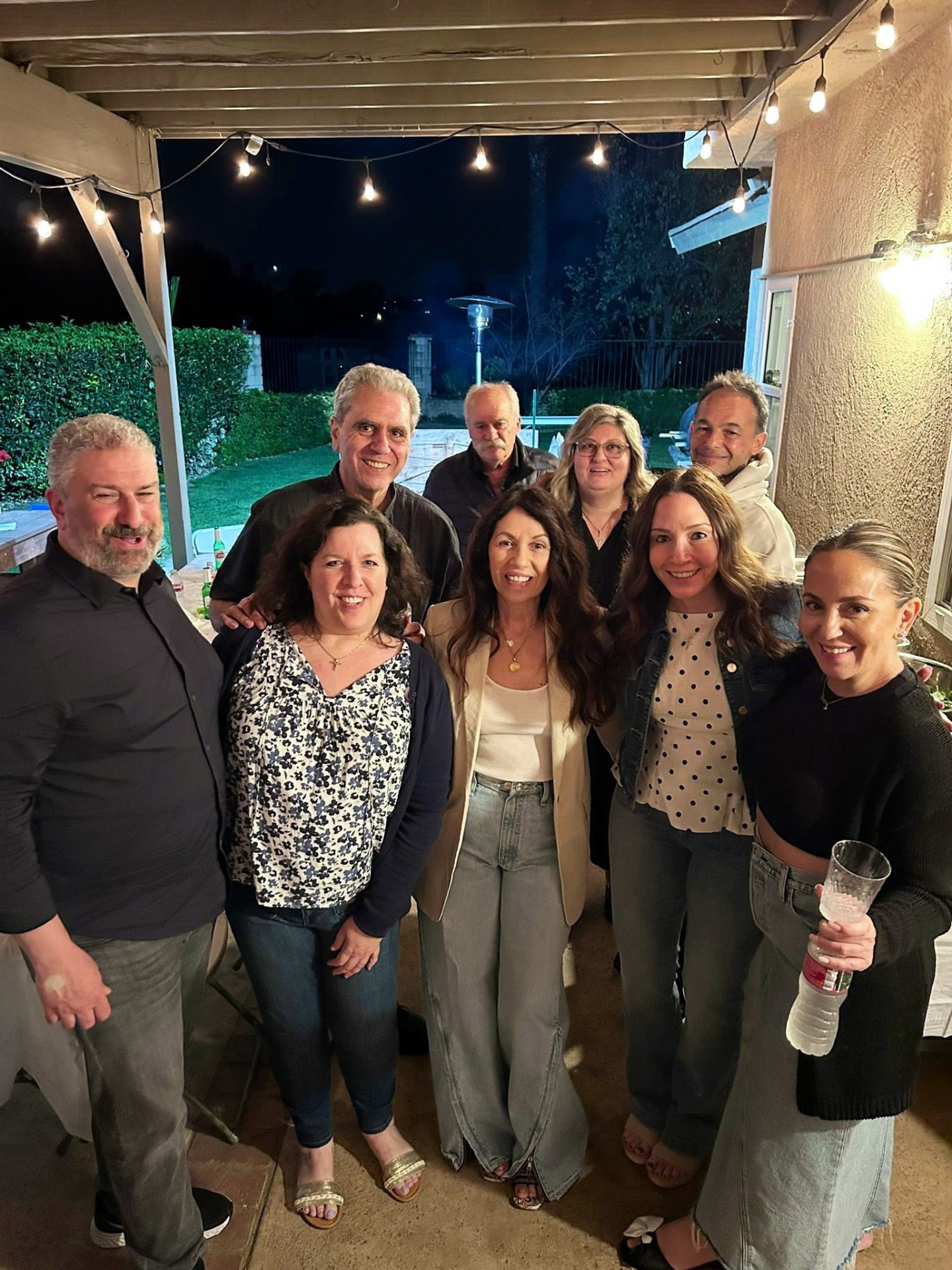 Members posing together outdoors under string lights at an evening gathering