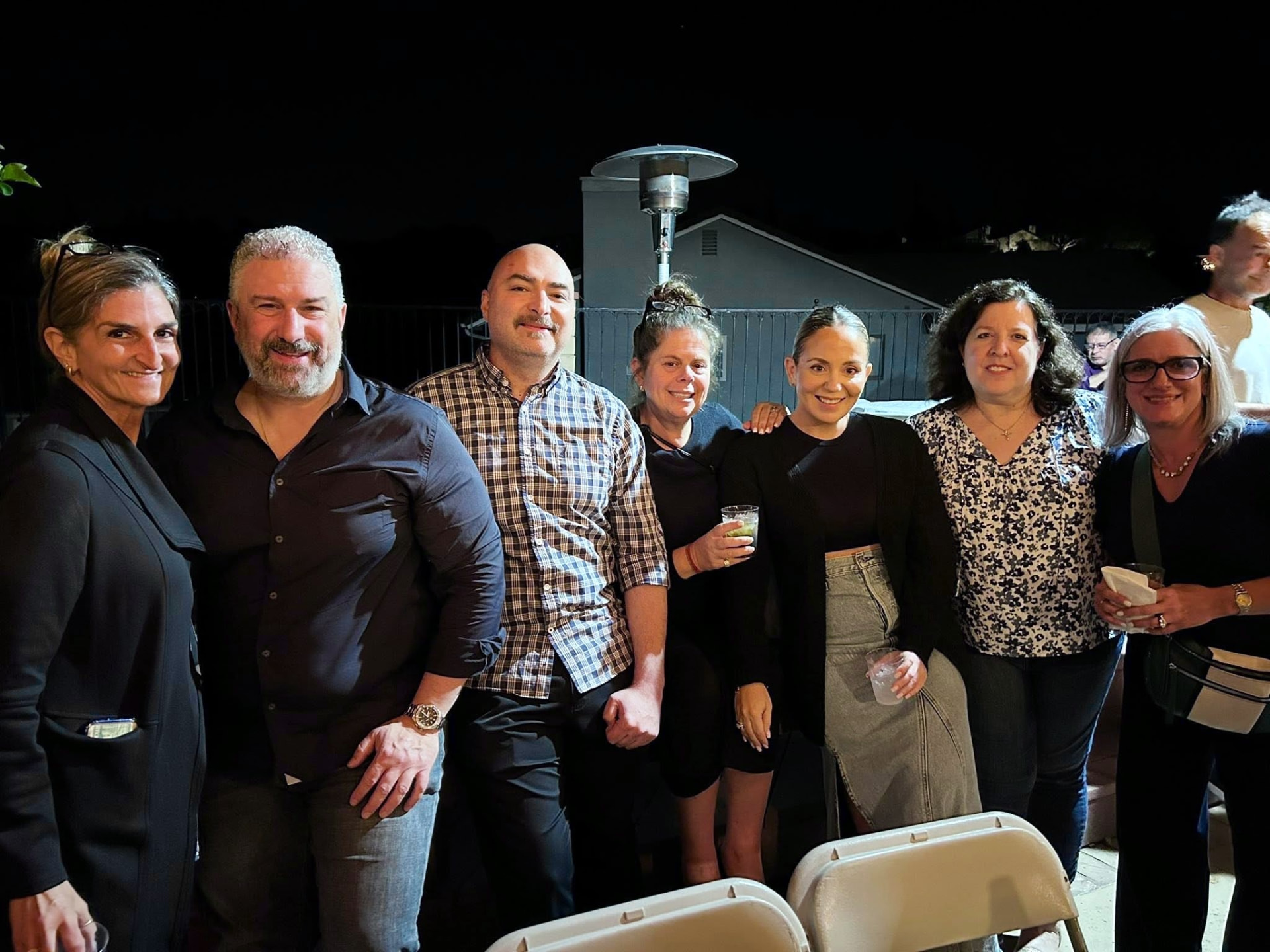 Members posing together outdoors with drinks at an evening gathering